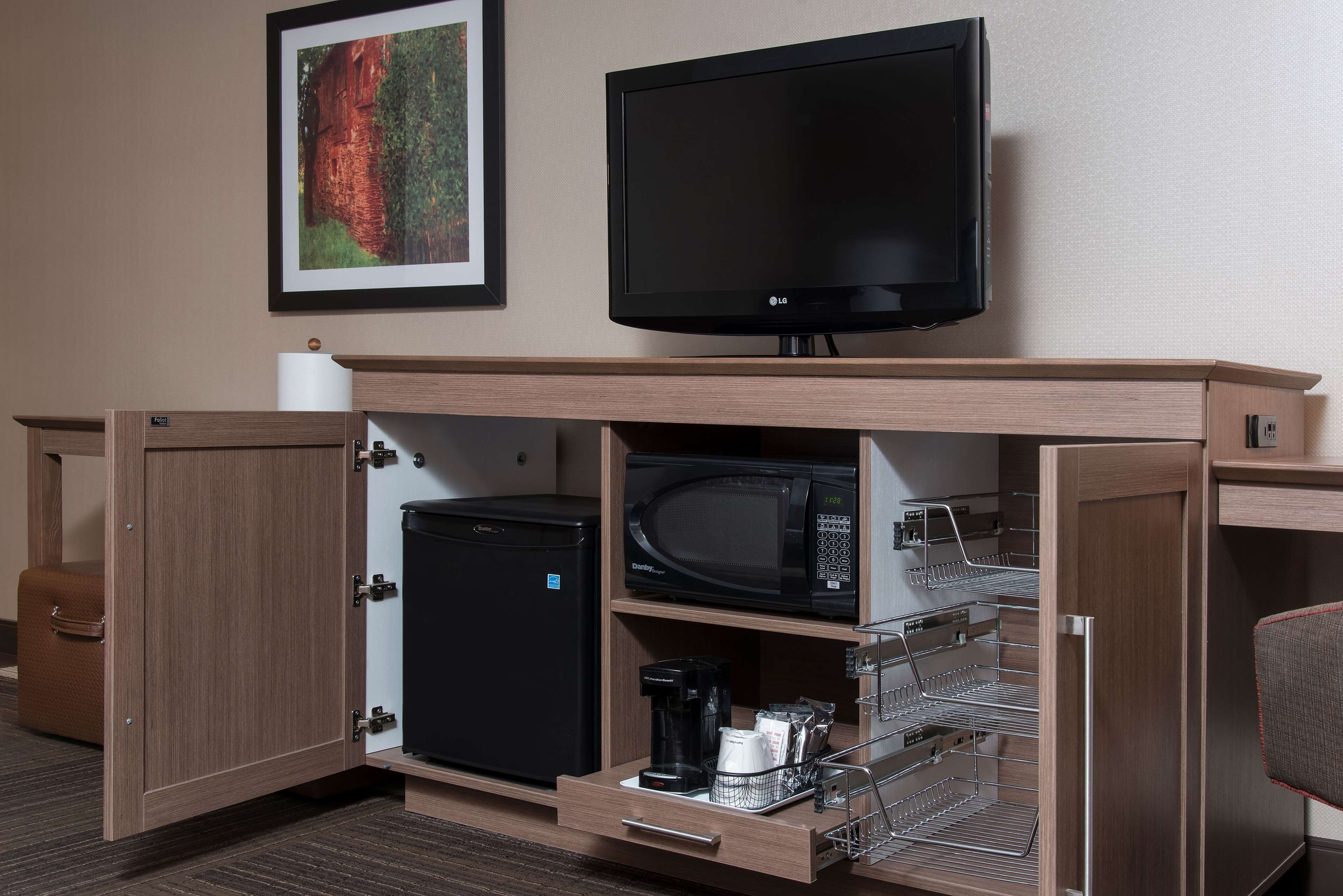 A compact hotel room with a flat-screen TV, a microwave, a mini-fridge, a coffee maker, and a small cabinet.