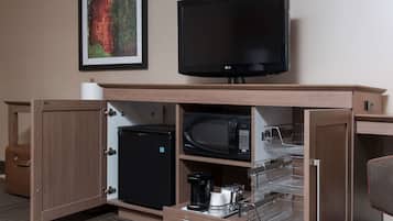 A compact hotel room with a flat-screen TV, a microwave, a mini-fridge, a coffee maker, and a small cabinet.