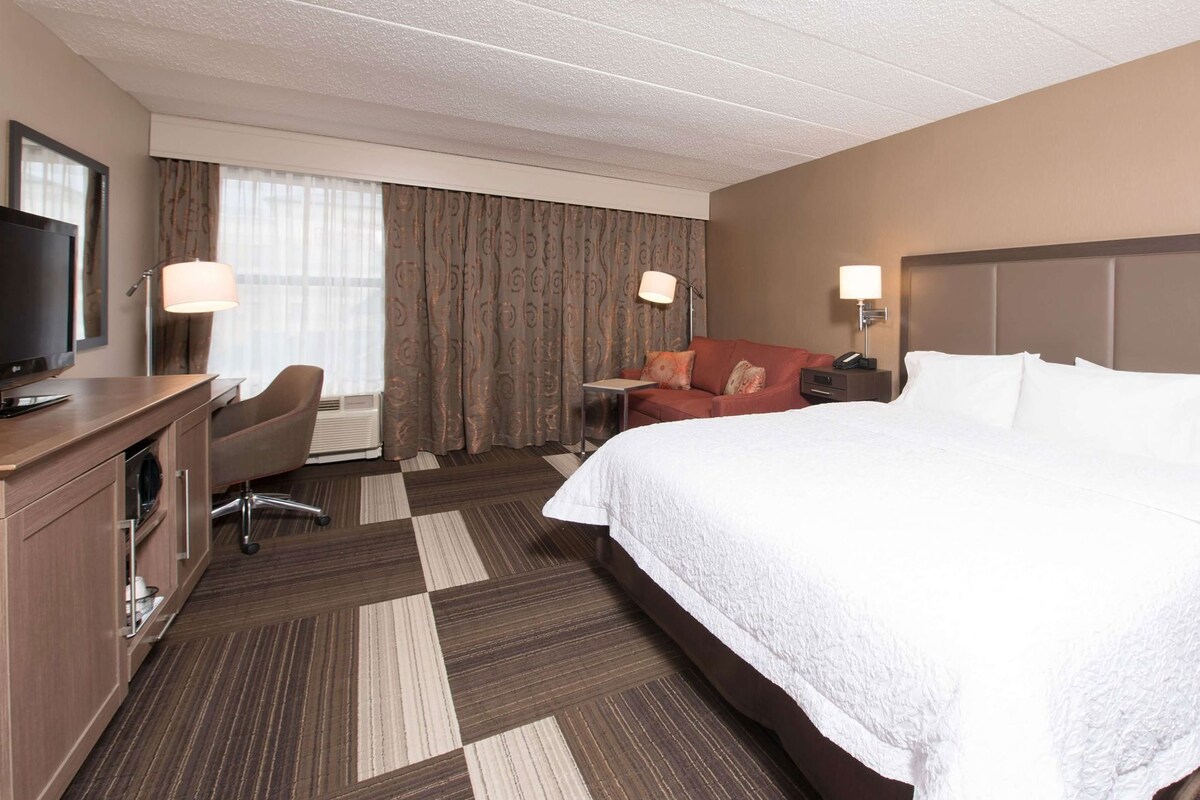 A hotel room with a bed, a desk, a chair, a TV, and a window with curtains.