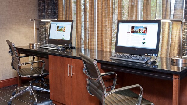 A modern office space with two laptops on a glass desk, two office chairs, and a view through large curtains. - Hampton Inn Columbus/Taylorsville/Edinburgh (Edinburgh)