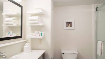 A bathroom with a white sink, mirror, and shelves with towels and toiletries.