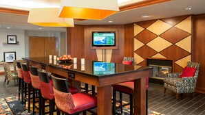 A hotel lobby with a long wooden reception desk, red upholstered bar stools, a flat-screen TV mounted on the wall, and a patterned wall design. - Hampton Inn Columbus/Taylorsville/Edinburgh (Edinburgh)