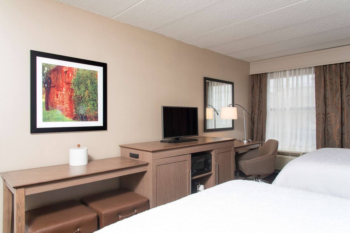 A hotel room with a bed, a desk with a television, a chair, a microwave, and a framed picture on the wall.