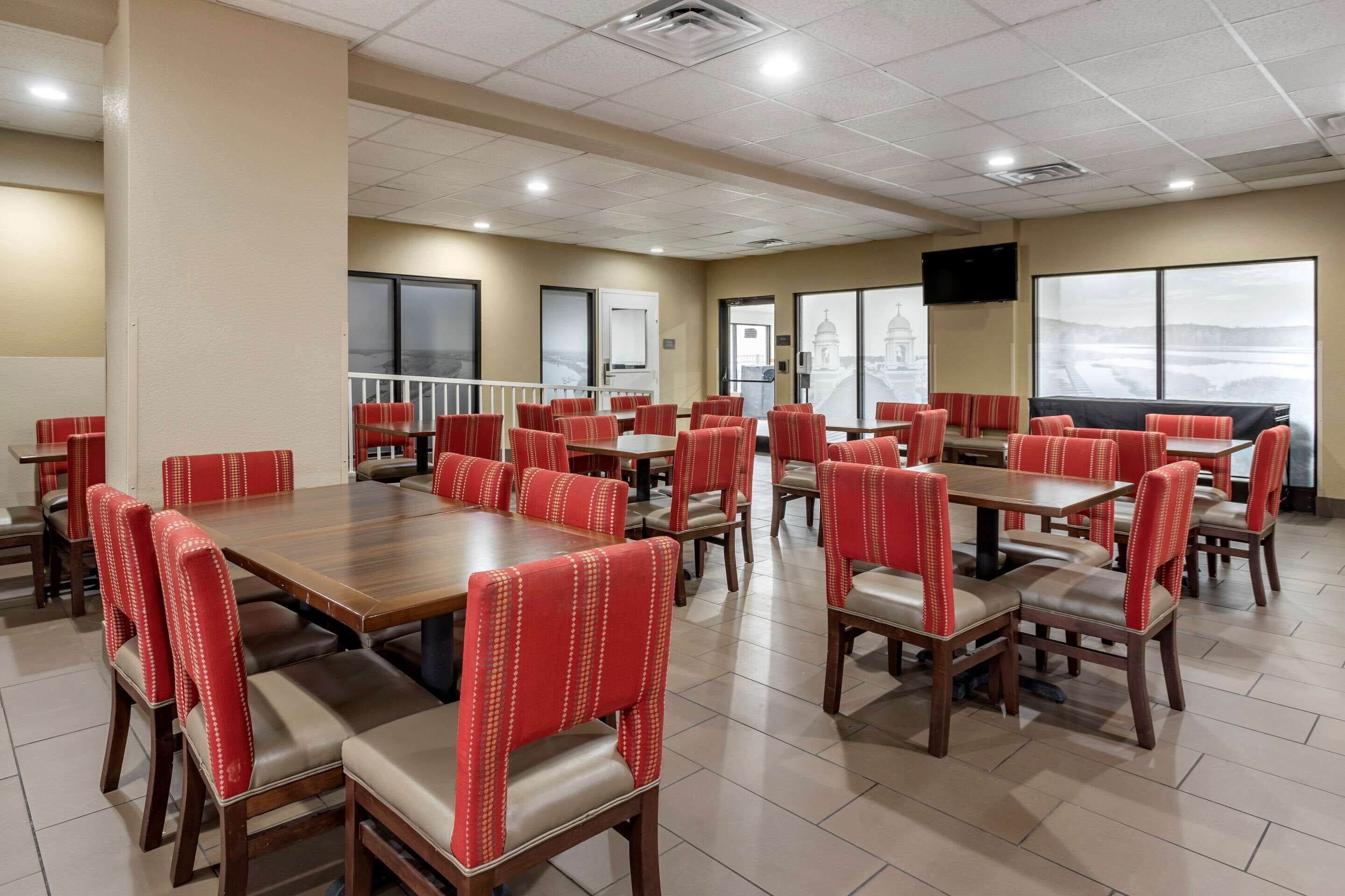 A spacious dining area with multiple tables and chairs, large windows with a view, and a flat-screen TV mounted on the wall.