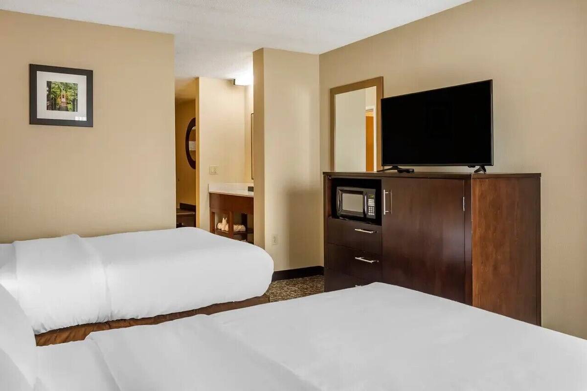A hotel room with two beds, a TV, a microwave, and a mirror.
