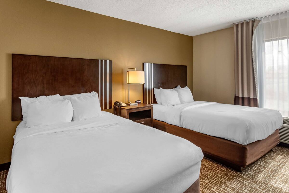 A hotel room with two beds, a nightstand with a lamp, and a window with curtains.
