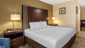 Habitación de hotel con una cama grande, una mesita de noche con una lámpara, un escritorio con una silla y un cuadro en la pared.