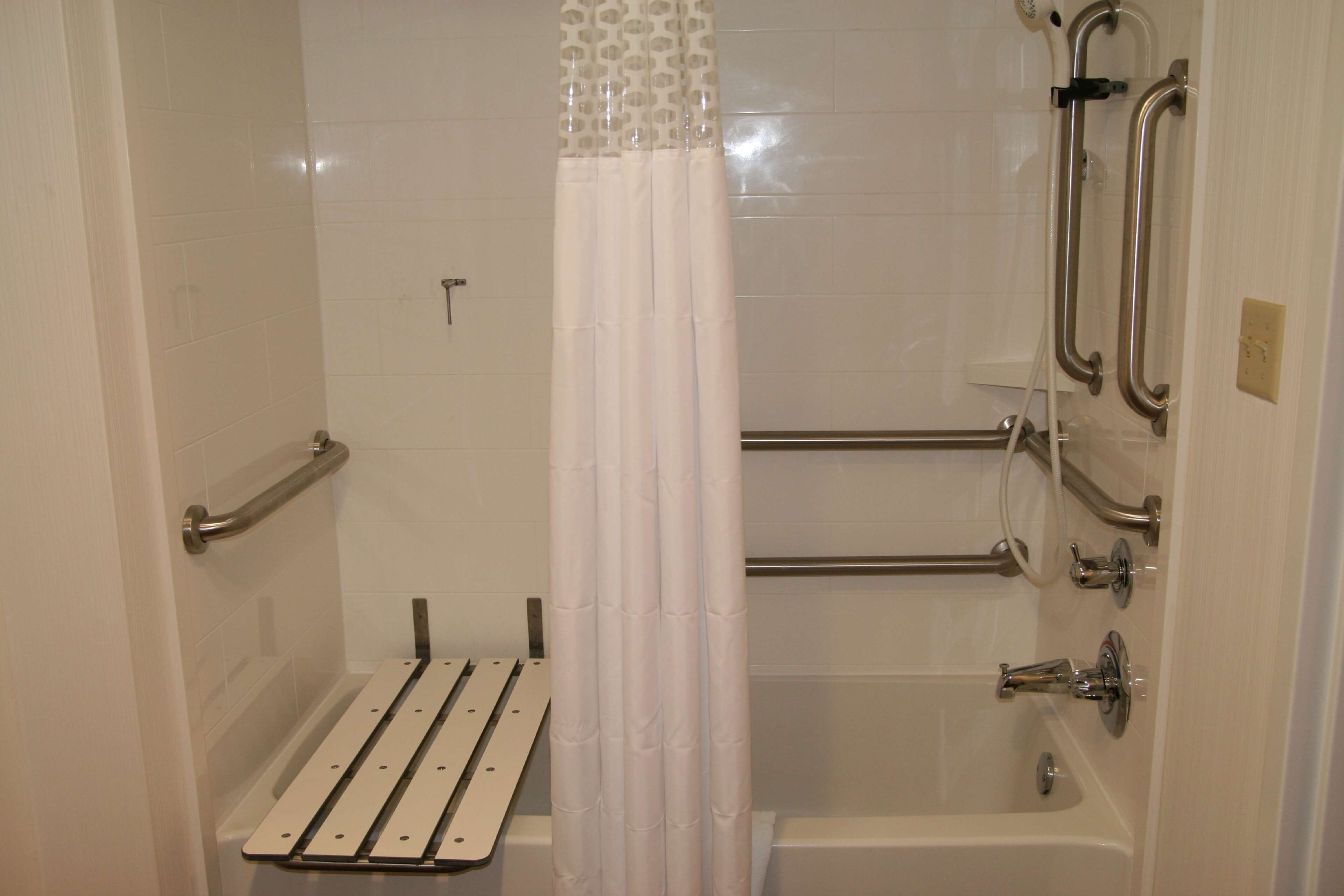 Un baño con ducha, barras de apoyo y un asiento.