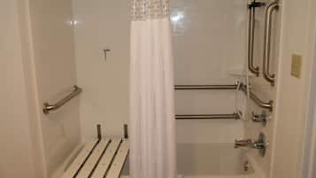 Un baño con ducha, barras de apoyo y un asiento.