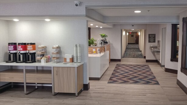 Eine Hotelhalle mit Kaffeeangebot, einer Rezeption und einer Treppe zu weiteren Bereichen.