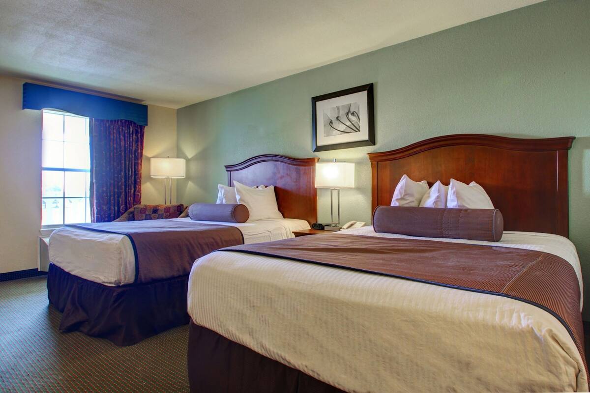 A hotel room with two beds, a framed picture on the wall, and a window with curtains.