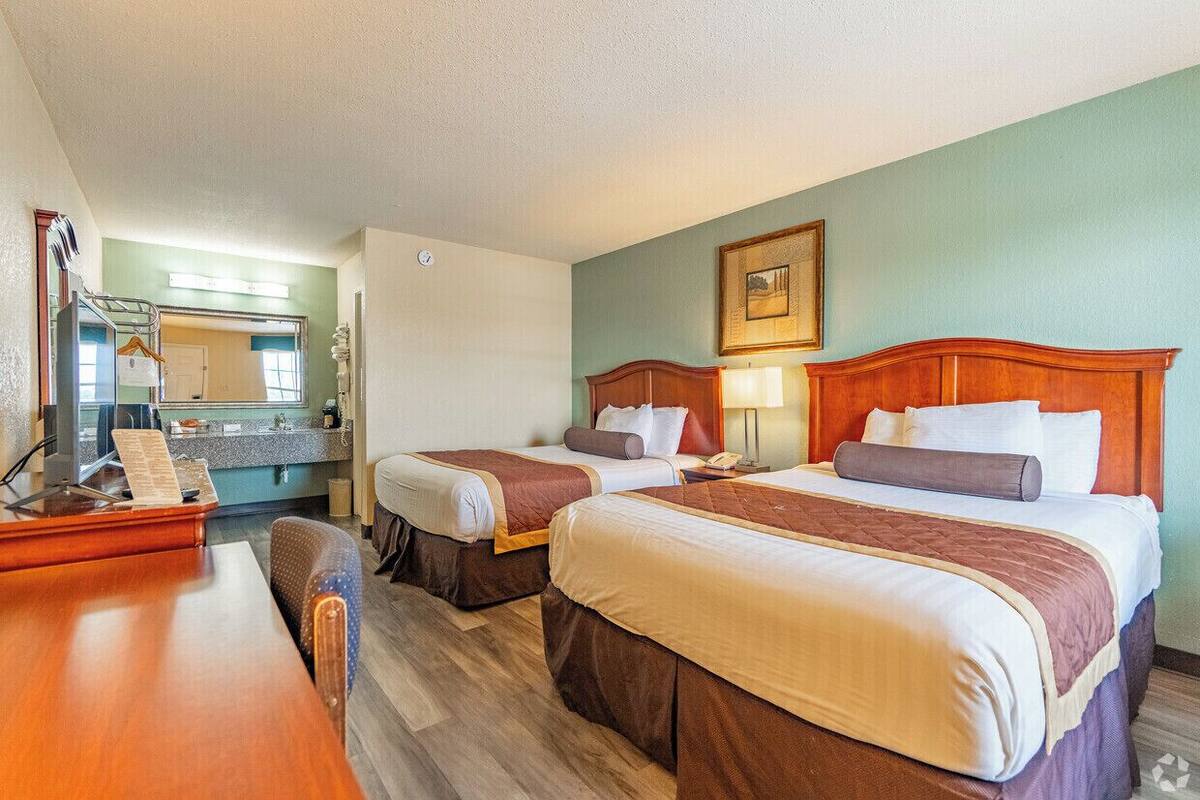 A hotel room with two beds, a desk, and a mirror.