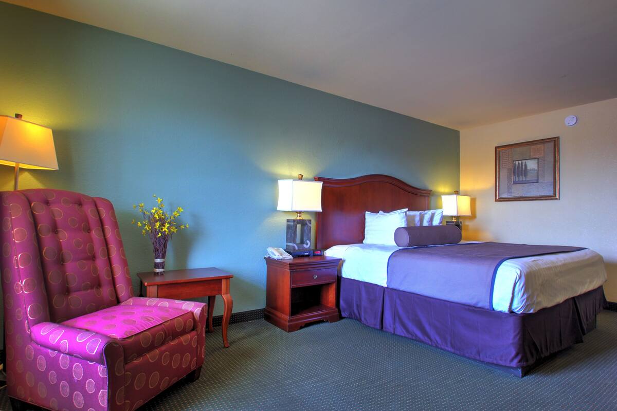 A hotel room with a bed, a chair, a nightstand, and two lamps.