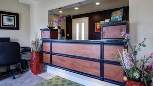 A reception desk with a sign for KeyWest Inn, a black office chair, and a red planter with flowers. - Key West Inn Tunica (Robinsonville)