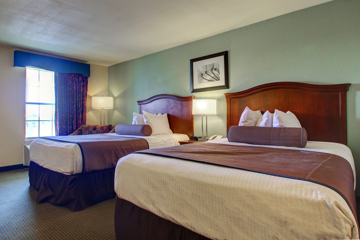 A hotel room with two beds, a window with curtains, a framed picture on the wall, and a lamp on each side of the beds.