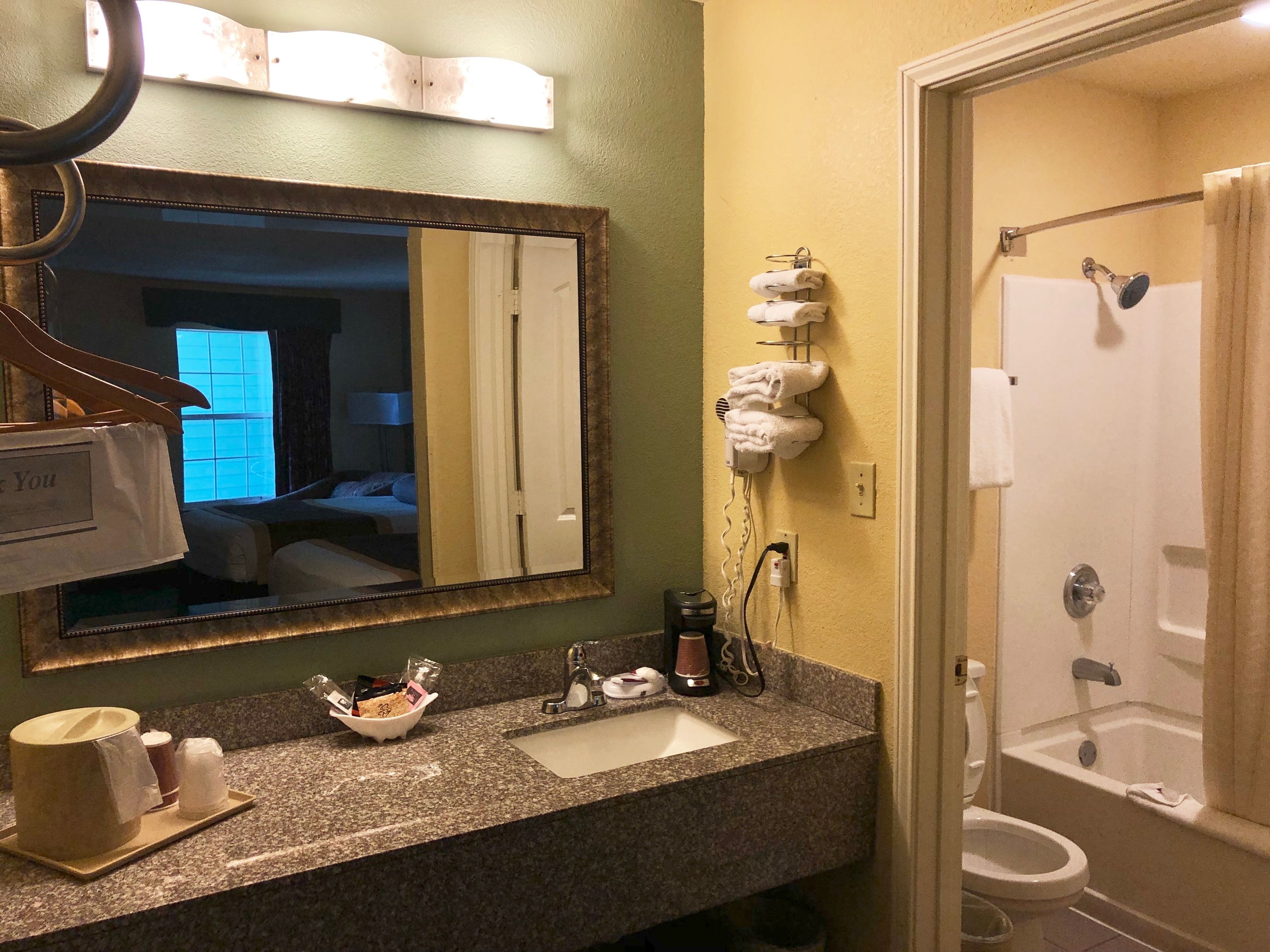 A bathroom with a granite countertop, a sink, a mirror, and a shower area.