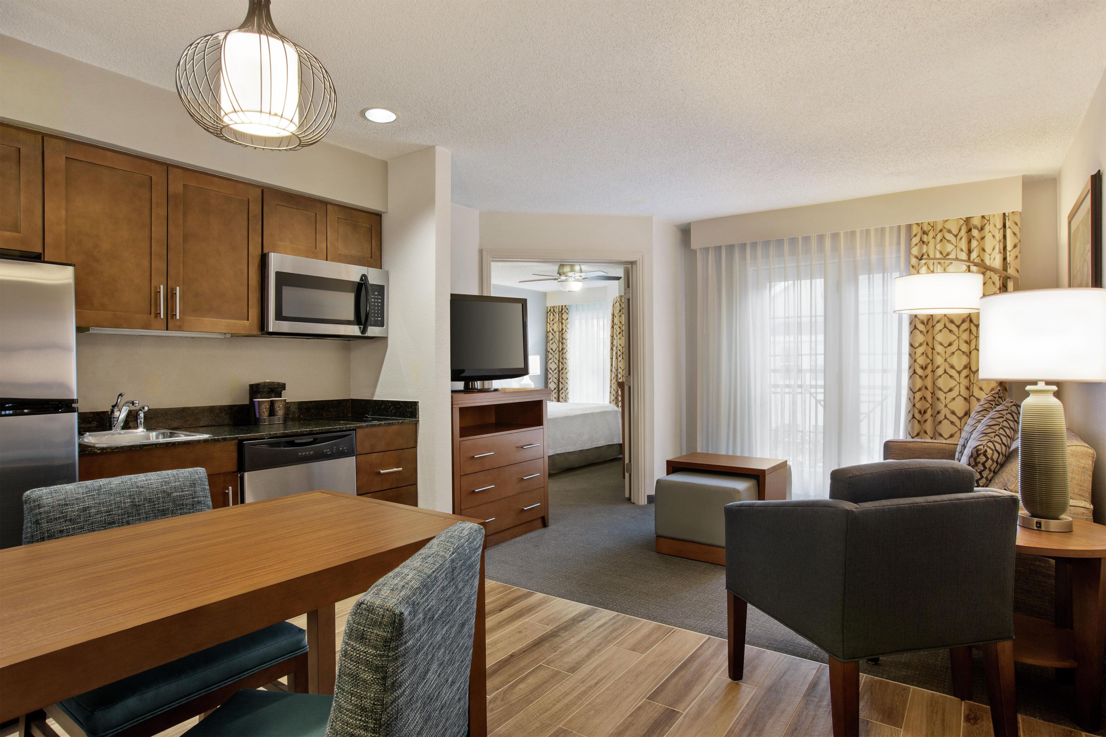A compact hotel room with a kitchenette, a dining area, a living space, and a television.