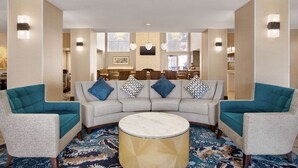 A hotel lobby with a curved sofa, two armchairs, a round coffee table, and a patterned carpet. - Homewood Suites by Hilton Kansas City-Airport (Kansas City)
