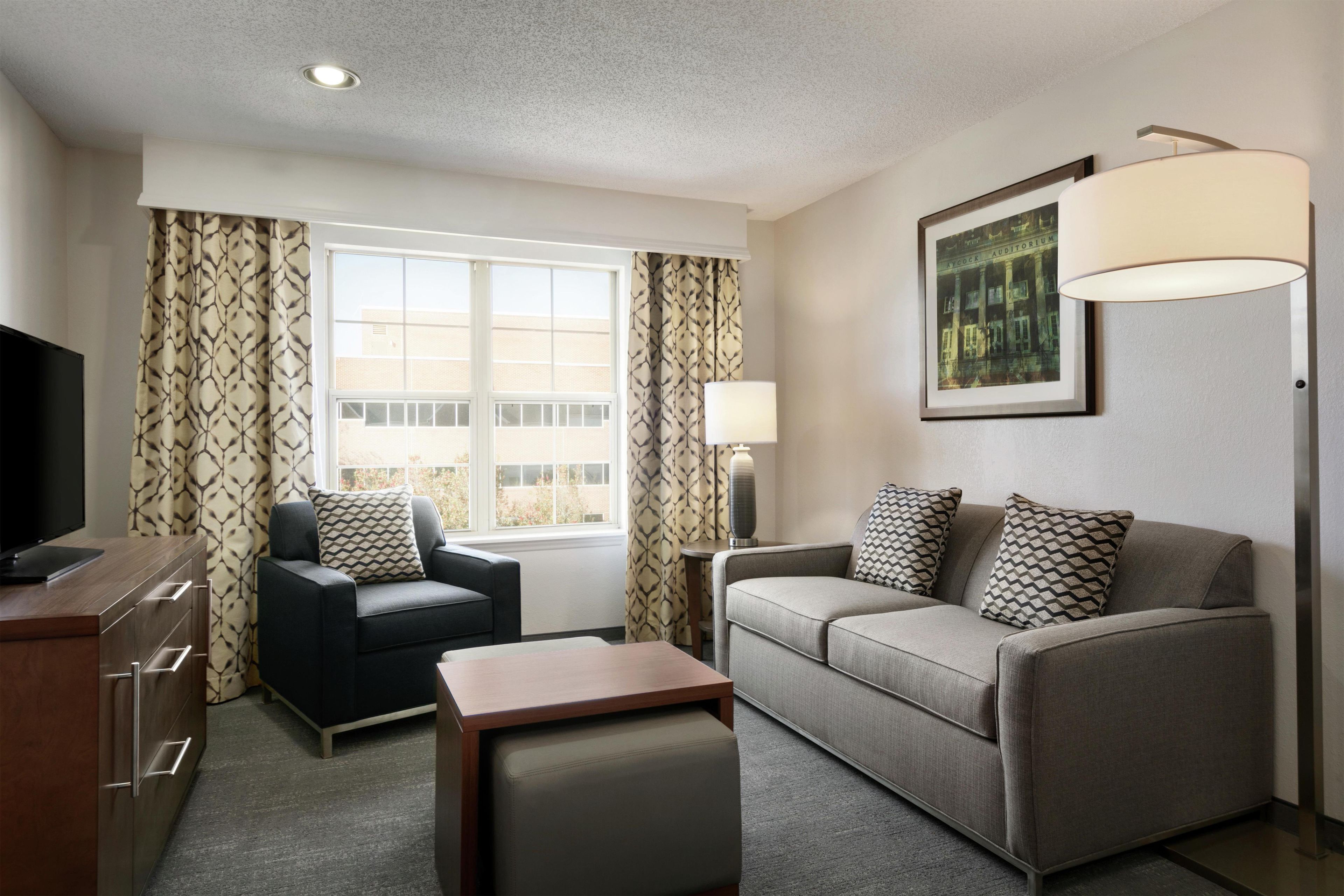 A hotel room with a sofa, armchair, TV, and a framed picture on the wall.