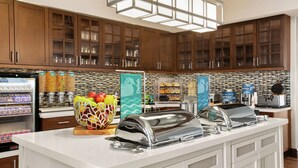 A hotel kitchen with a buffet setup, including a fruit bowl, a toaster, and a waffle maker. - Homewood Suites by Hilton Kansas City-Airport (Kansas City)