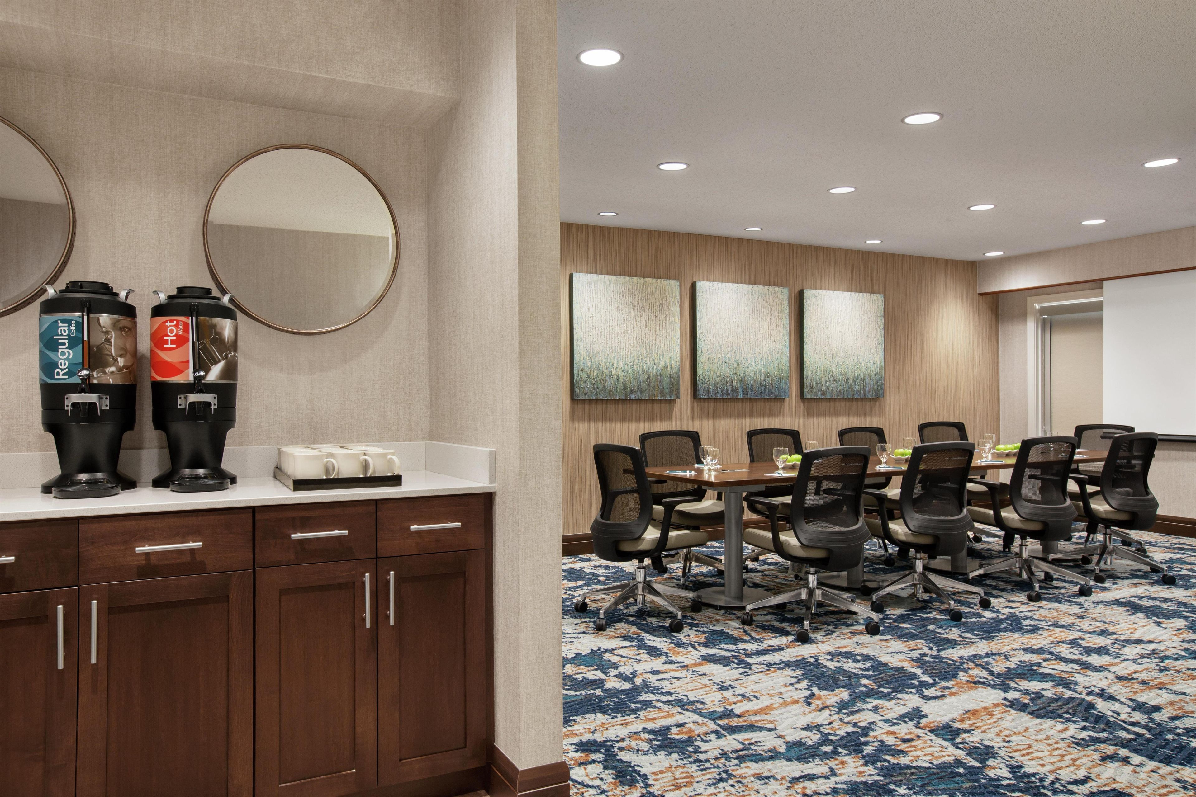 A conference room with a long table, chairs, a coffee station, and artwork on the wall.