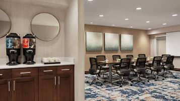 A conference room with a long table, chairs, a coffee station, and artwork on the wall.