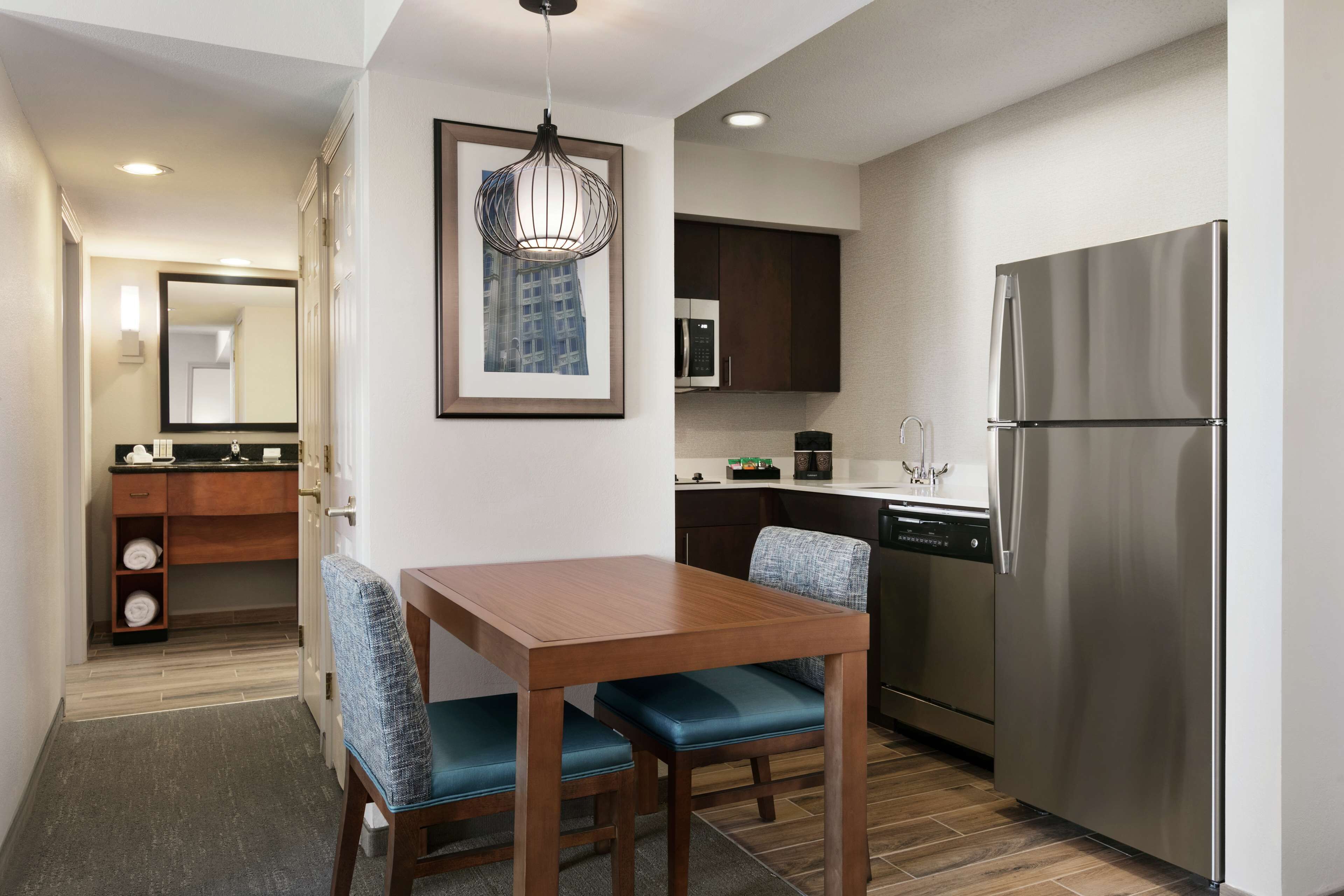 Una cocina moderna con un refrigerador de acero inoxidable, una mesa de comedor de madera con sillas azules, y un cuadro en la pared.