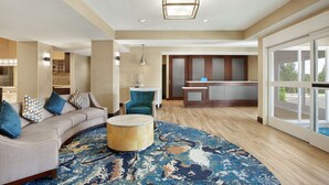 A modern hotel lobby with a curved sofa, a round coffee table, and a patterned rug. - Homewood Suites by Hilton Kansas City-Airport (Kansas City)