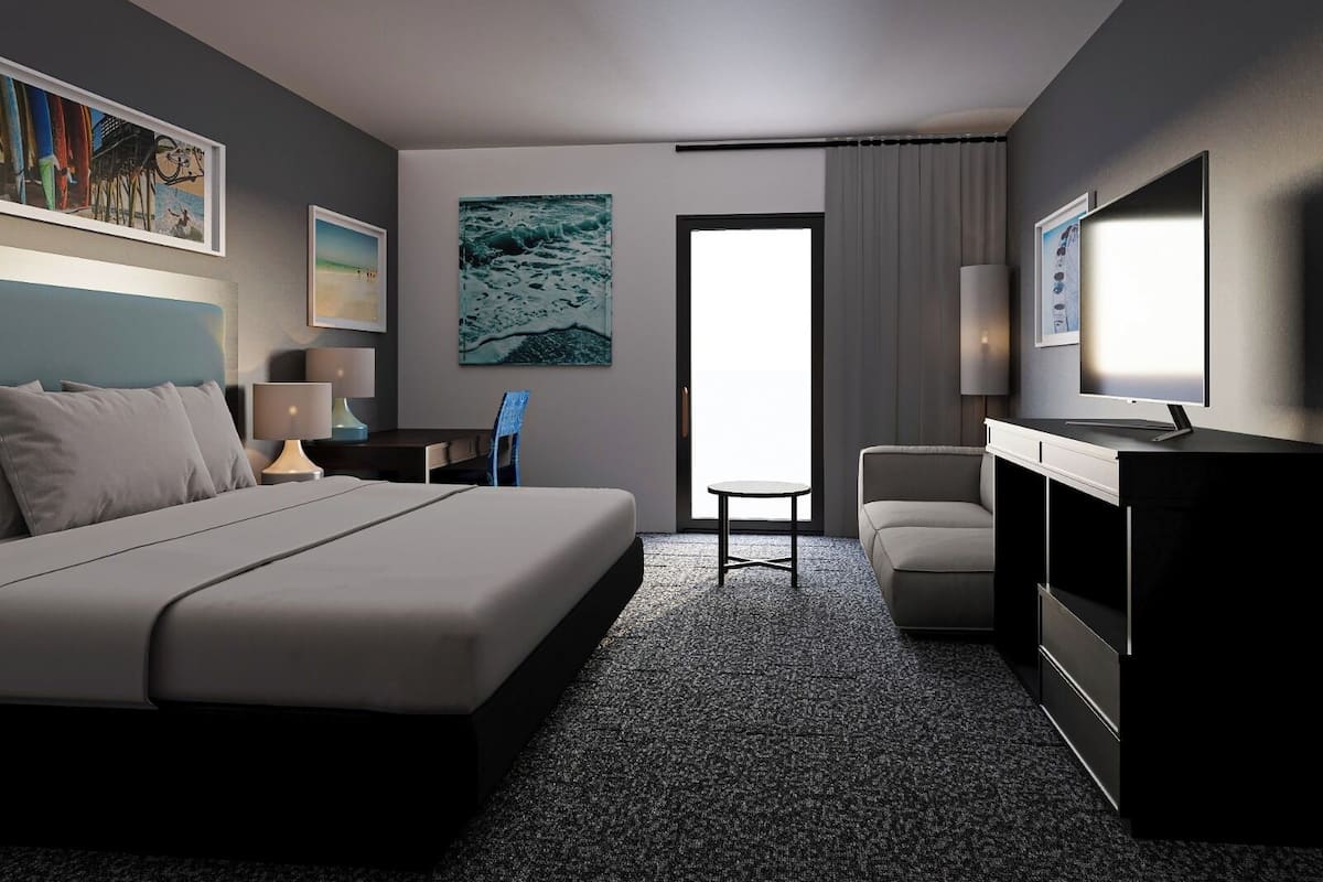 A hotel room with a bed, a desk, a chair, a TV, and artwork on the walls.