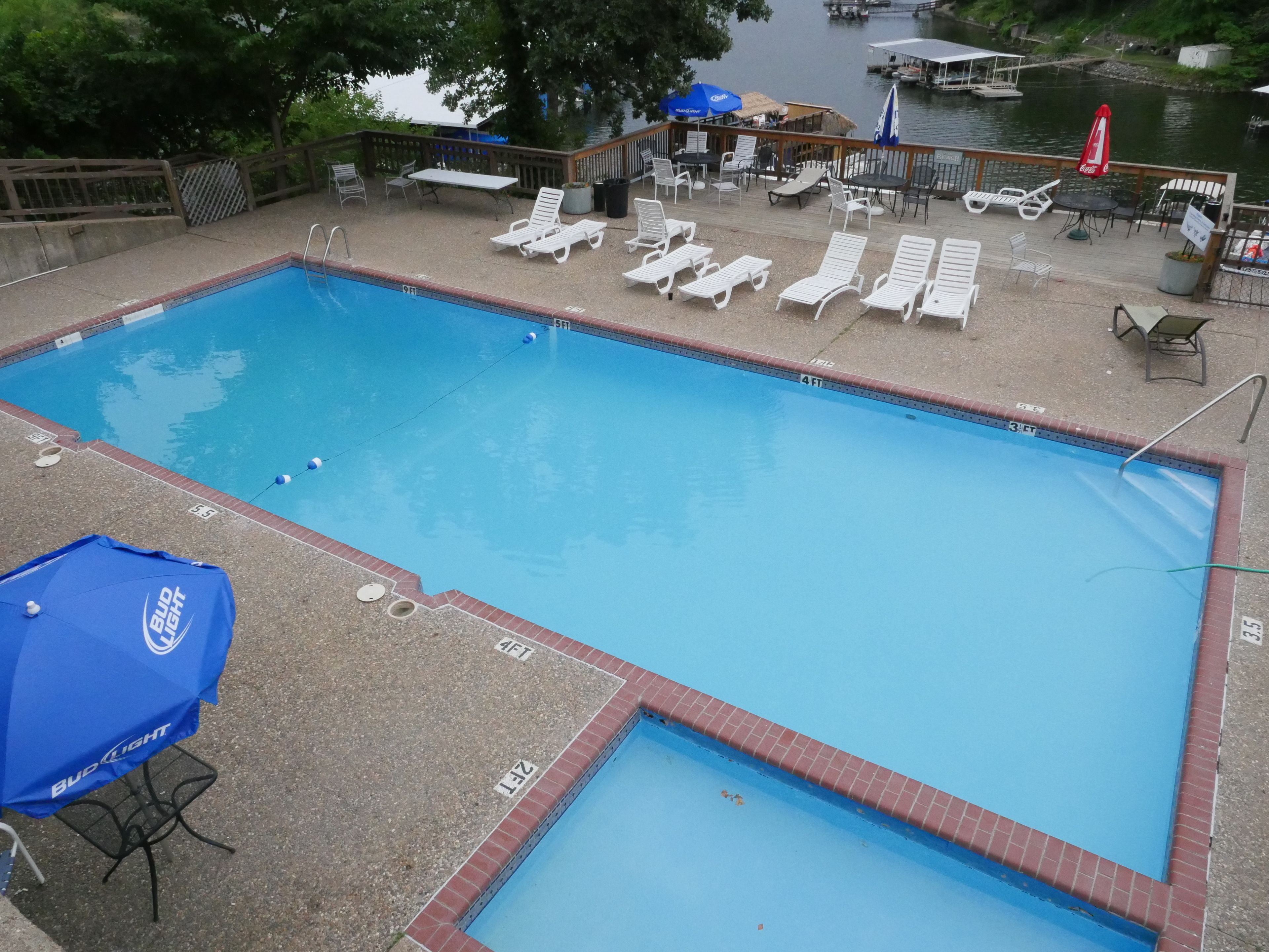 A rectangular swimming pool with a brick edge, surrounded by lounge chairs and umbrellas.