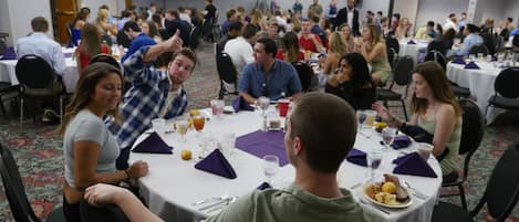 Un salón de conferencias con mesas redondas, sillas y asistentes sentados.