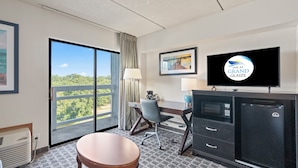 A hotel room with a large window, a desk, a chair, a television, and a minibar.