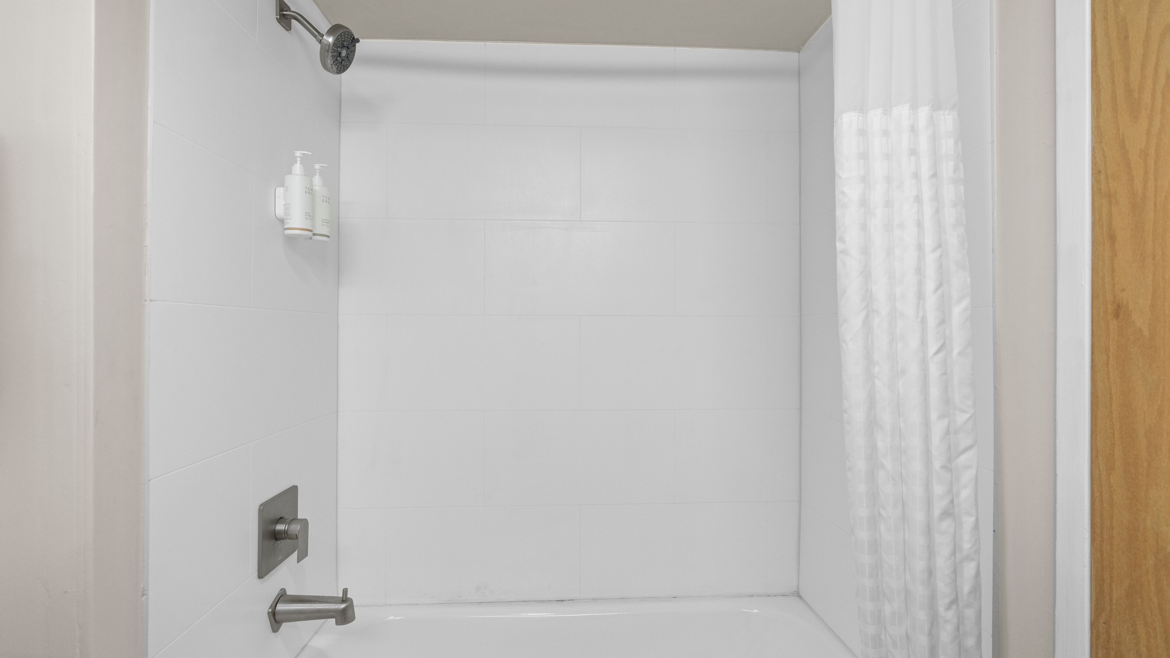 Et badeværelse med hvide fliser, en bruser og et toilet.