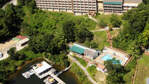 An aerial view of a large building with multiple floors, surrounded by greenery and a dock with boats.