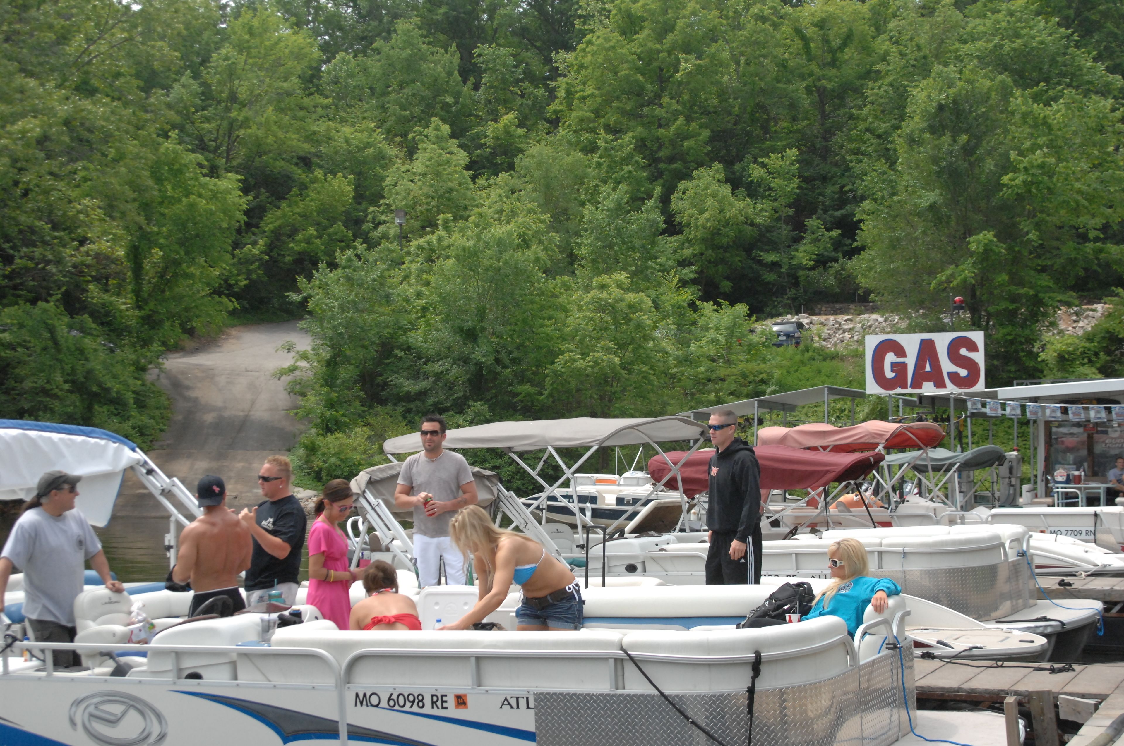 A marina with boats docked, a 'GAS' sign, and people around the boats.