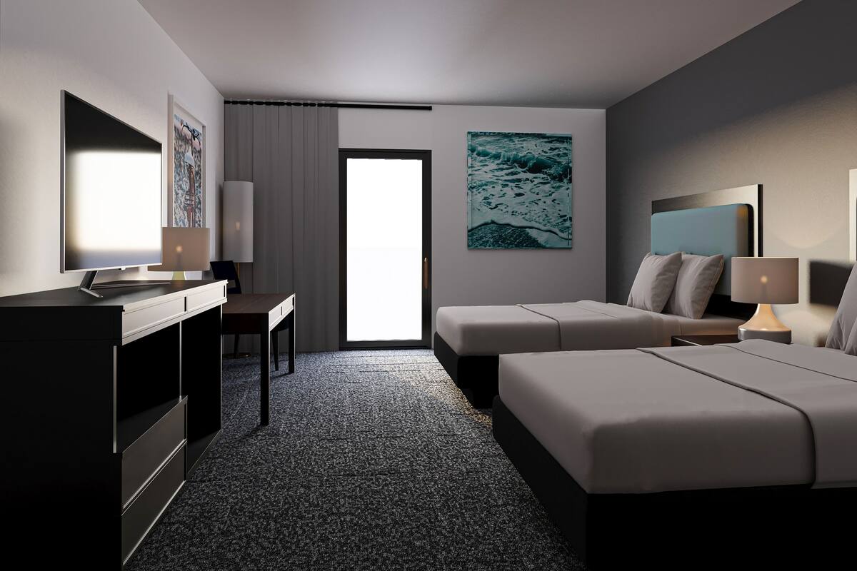 A hotel room with a desk, two beds, a large window, and artwork on the walls.