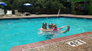 Una piscina con agua cristalina, marcas de profundidad y una zona de solárium con sillones de playa y sombrillas.