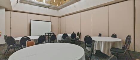 Un salón de conferencias con mesas y sillas redondas, una pantalla de proyector e iluminación empotrada en el techo.