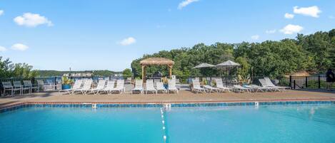 A swimming pool with lounge chairs and umbrellas, surrounded by a fence and trees.