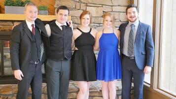 A group of people in formal attire standing indoors with a stone wall and wooden panel background.