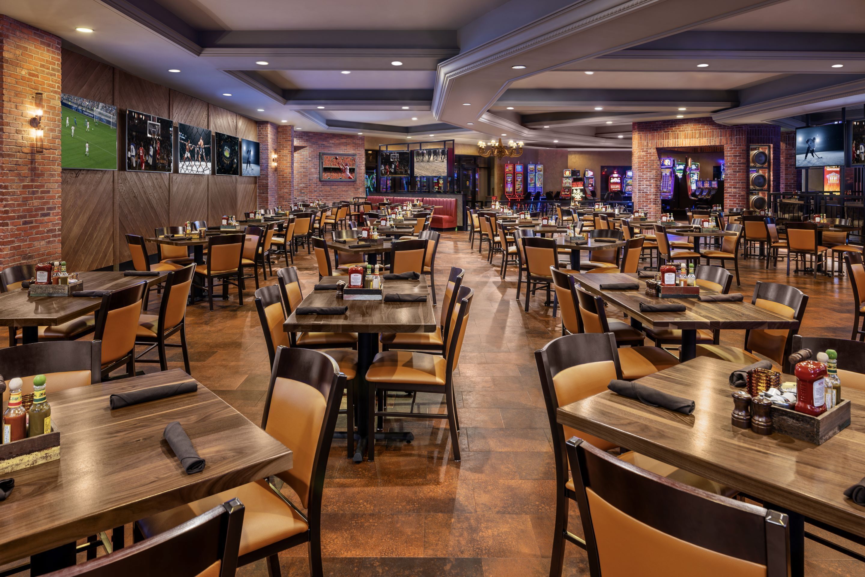 Um restaurante amplo com várias mesas e cabines, paredes de tijolo e objetos de coleção esportiva.