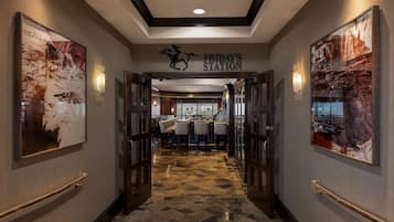 A hotel corridor with a bar area, framed artwork, and a sign reading "FRIDAY'S STATION".