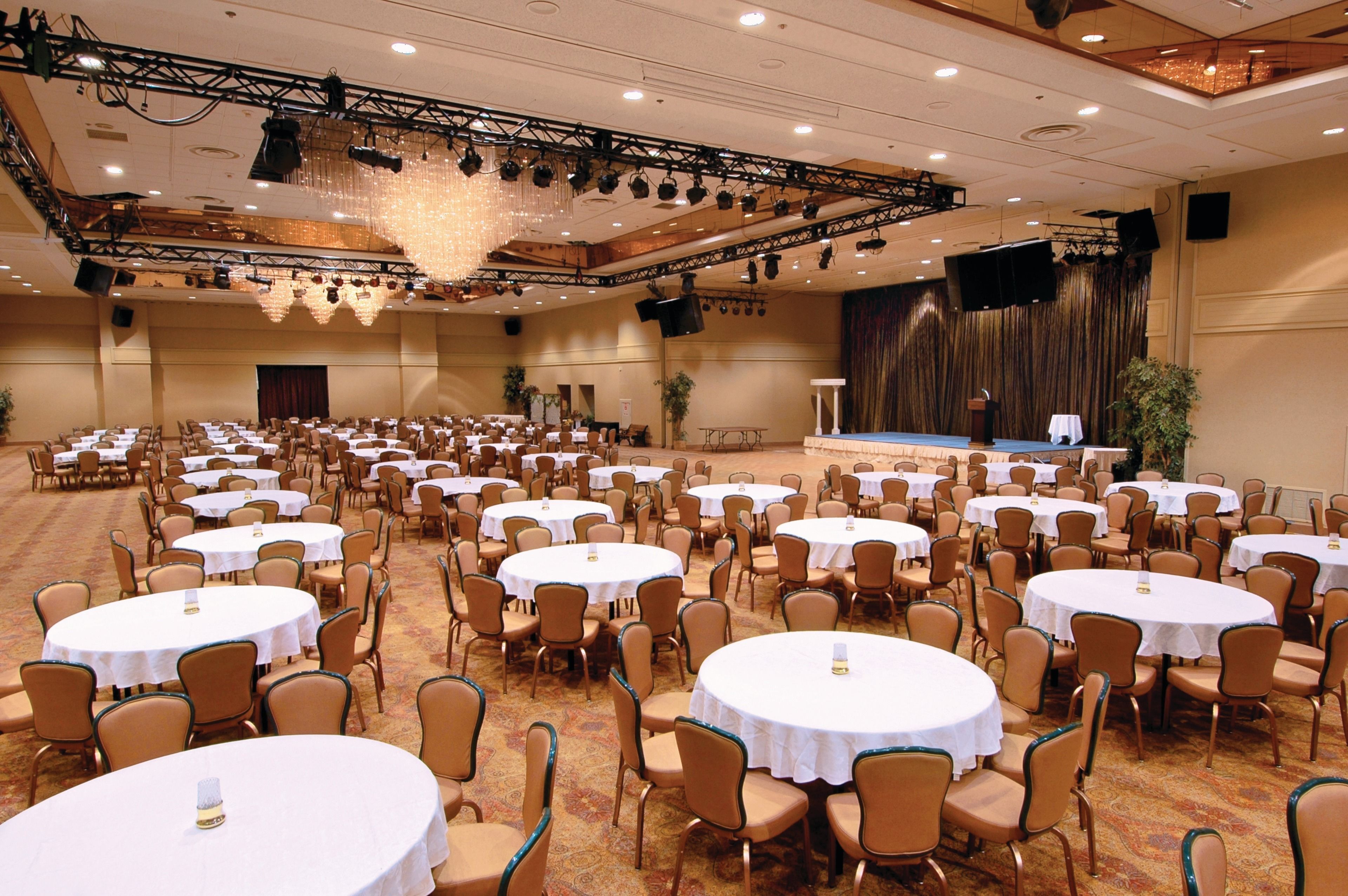 A large banquet hall with multiple round tables and chairs, a stage with a podium, and a large screen.