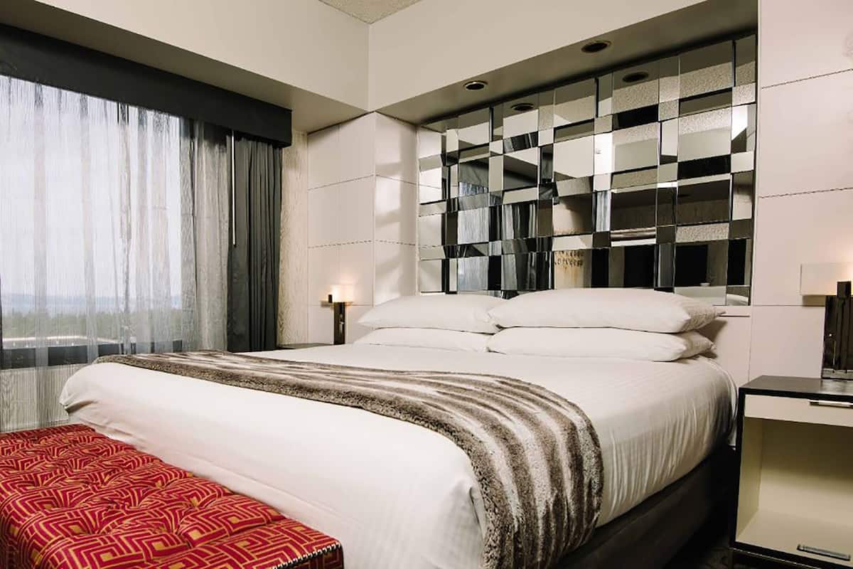 A hotel room with a large bed, a bedside table, a desk, and a window with curtains.