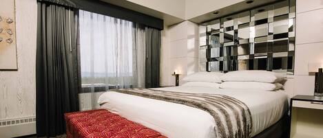 A hotel room with a large bed, a bedside table, a desk, and a window with curtains.