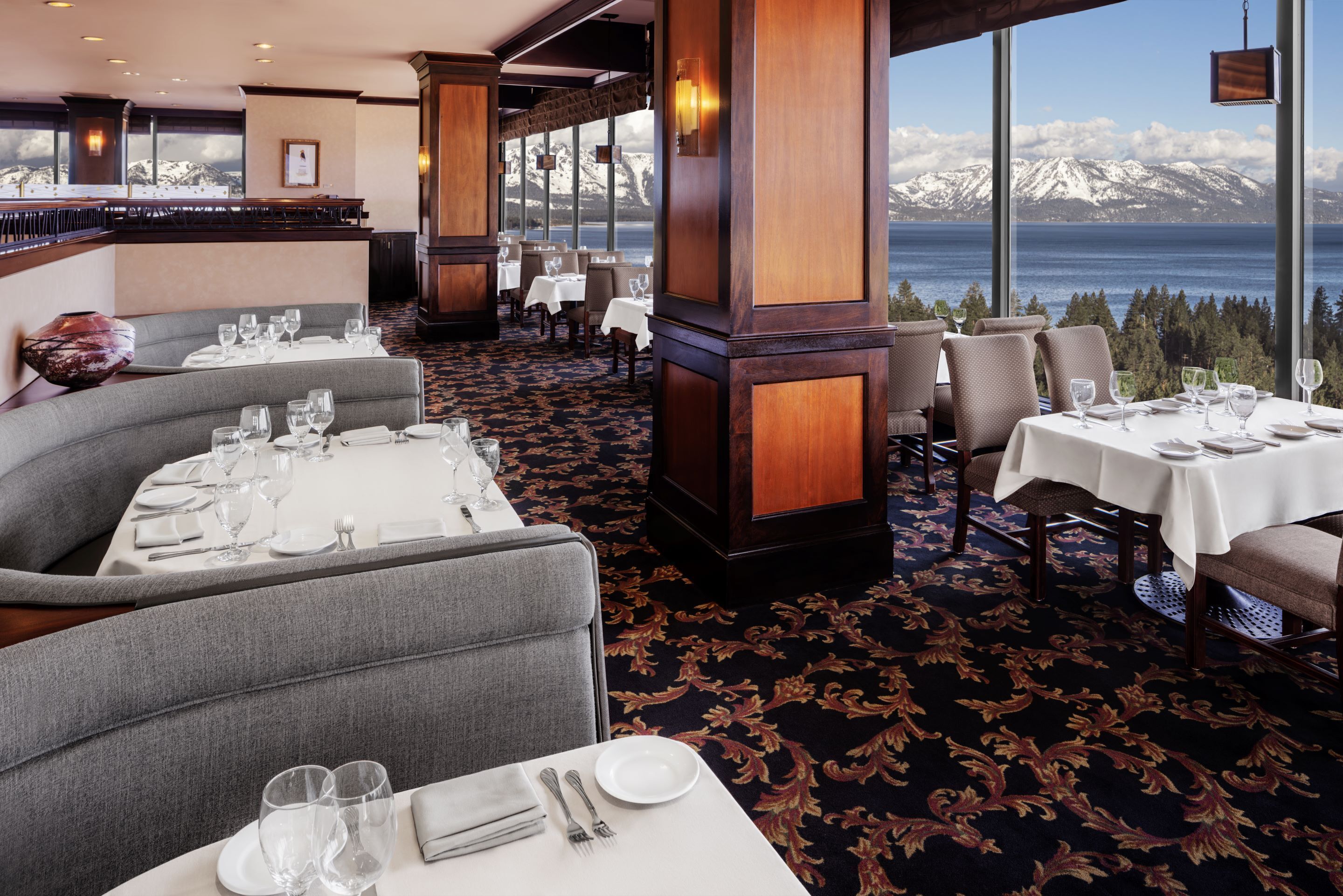 Un ristorante con tavoli apparecchiati per la cena, un'area bar e vista sulle montagne innevate.