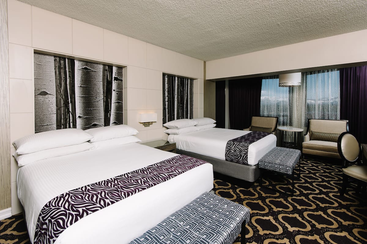 A hotel room with two beds, a sofa, a chair, and a view of the city.