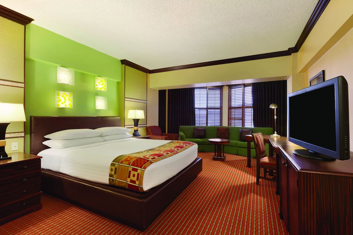 A hotel room with a large bed, green walls, a television, a desk, and a sofa.