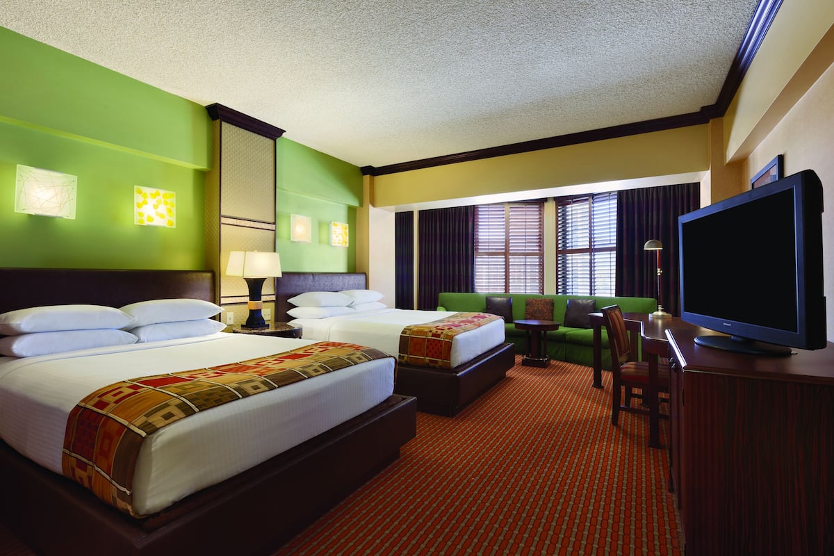 A hotel room with two beds, a green sofa, a television, and a desk.