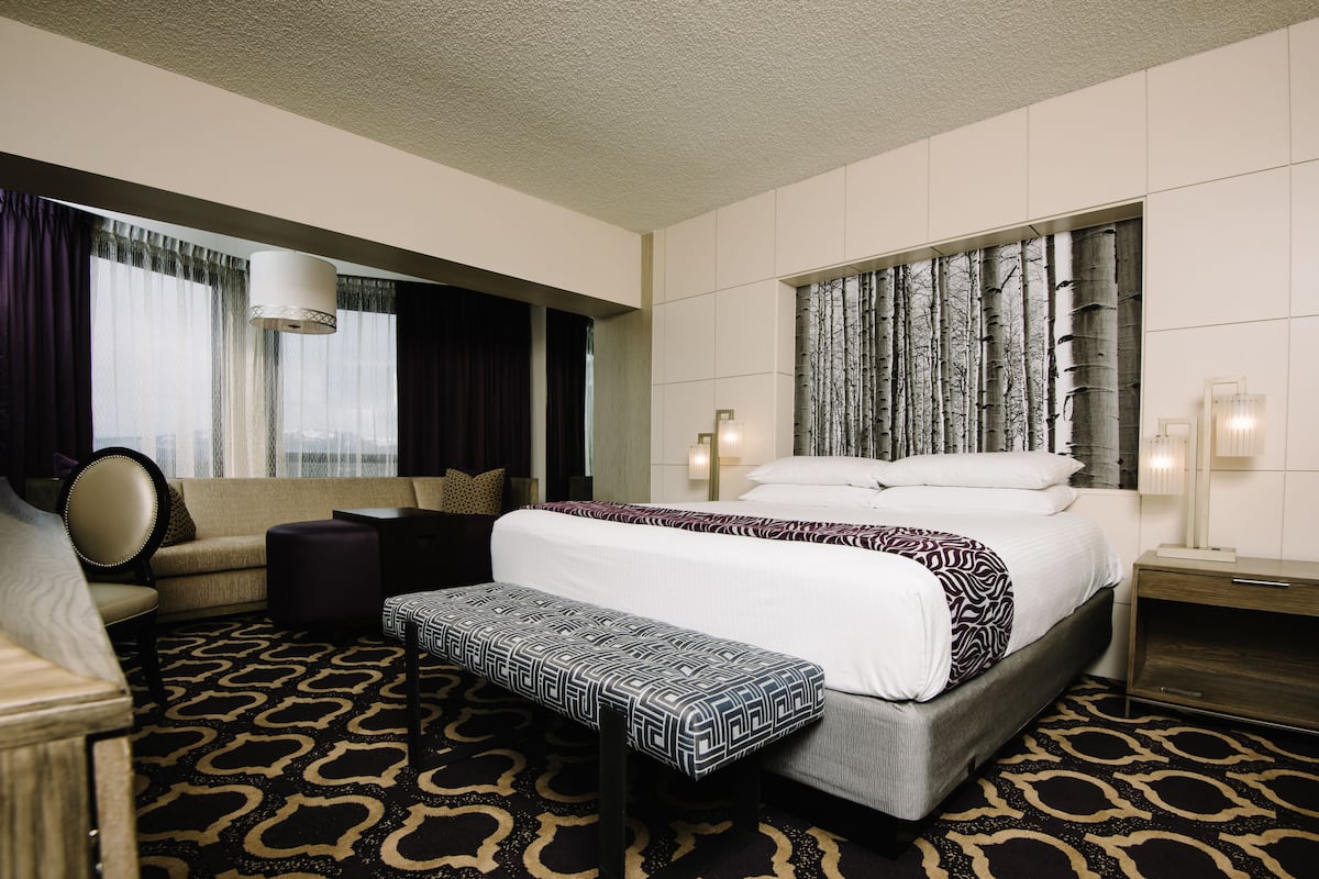 A hotel room with a large bed, a sofa, a bench, and a wall-mounted TV.